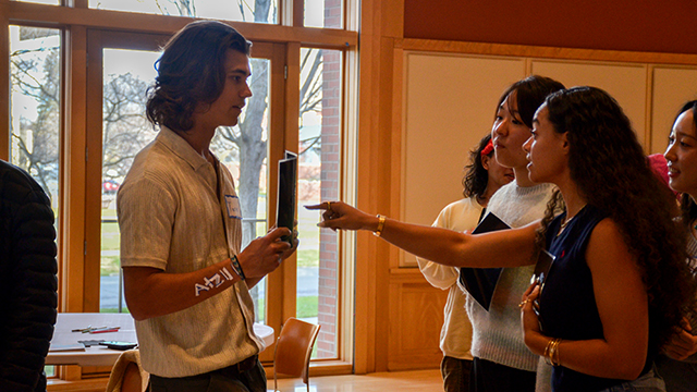 Several students on the right look and point at a piece of paper held by another student on the left.