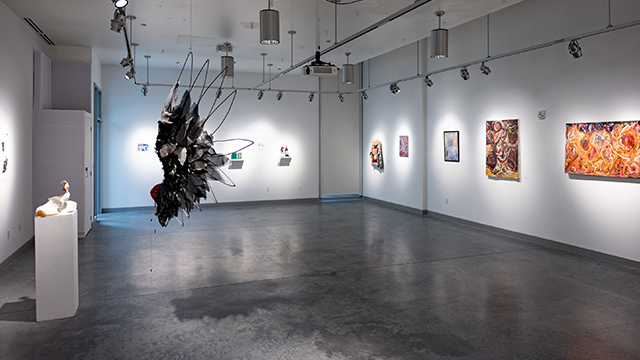 An art gallery space with cement floor and white lights illuminating artwork.