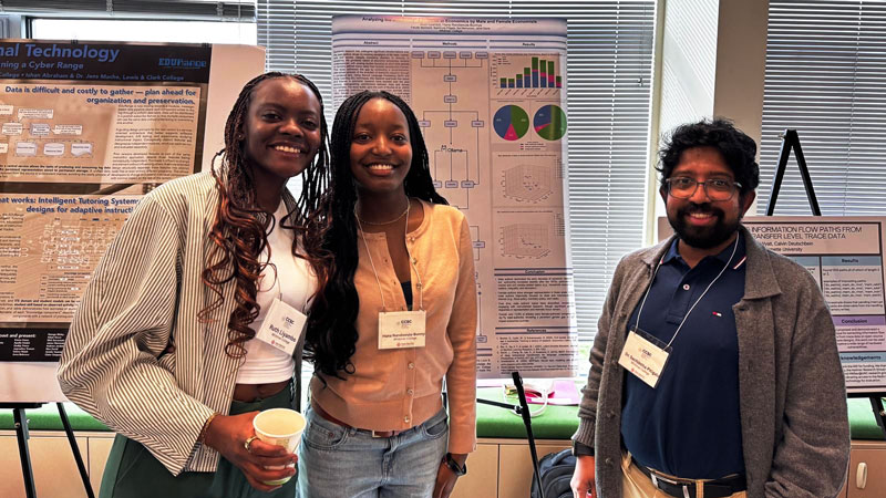 Ruth Iiyambo ’26 and Hana Nandawula-Bunnya ’28 pose in front of their research poster alongside Visiting Assistant Professor of Computer Science Sachintha Pitigala.