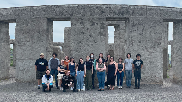 A group of people stand in front of a Stonehenge replica.