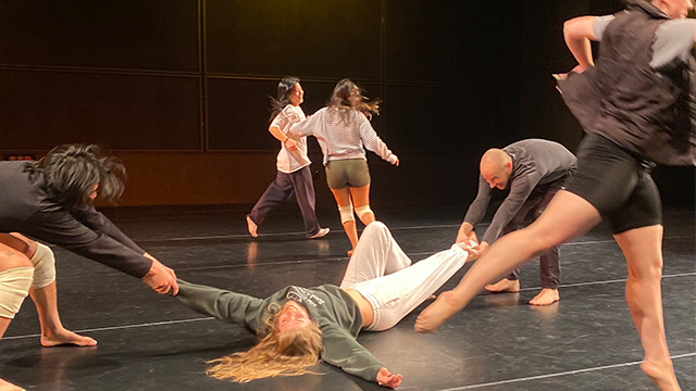 A chaotic scene with dancers rehearsing on a black stage.