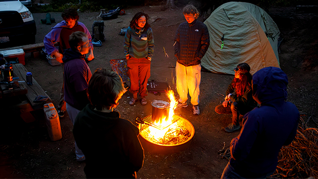 A group of students around a campfire at night.