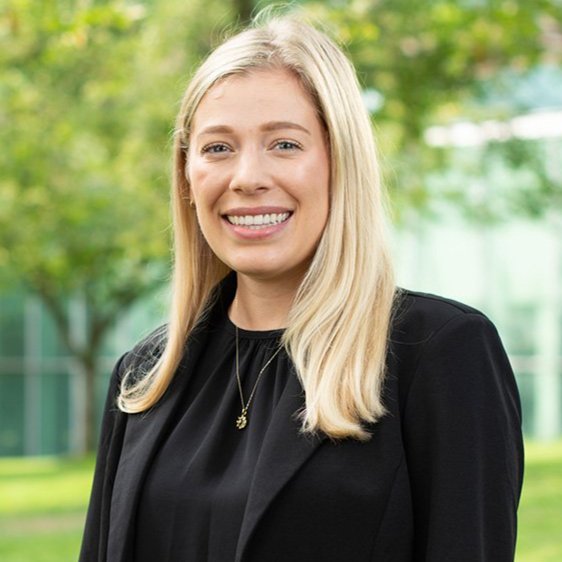 Chloe Young stands outdoors in front of a lawn, trees and a building