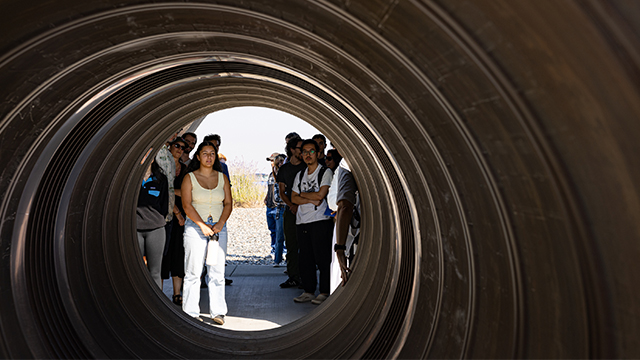 A group of people gathered outside of a very large pipe.