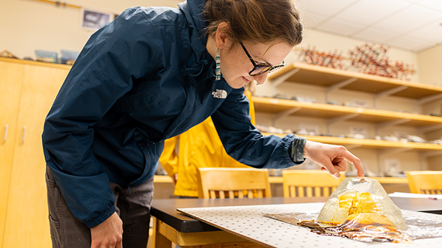 A student leans over a table and pokes at a mound of clear gelatin. 