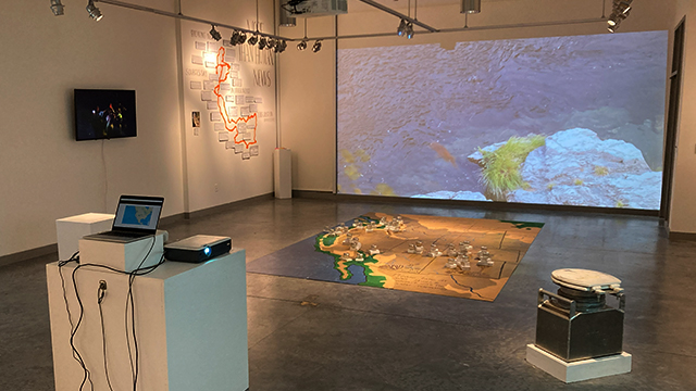 A gallery space with objects, projected images, and a large map on the floor.