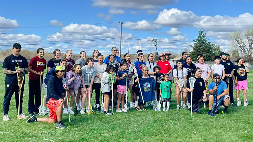 A large crowd of people, including adults and children, with many people holding lacrosse sticks.