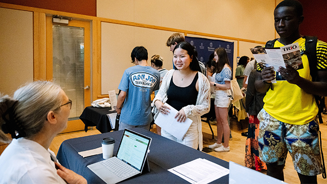 Students stop by tables where seated individuals are waiting to talk to them.