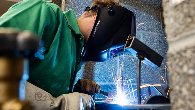 A student welding while wearing protective gloves and a helmet.