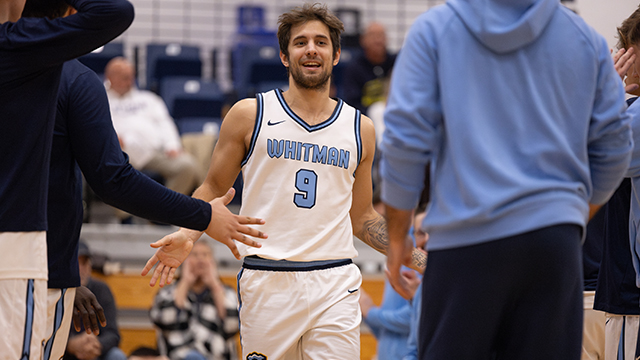 A Whitman men’s basketball player wearing the number “9” claps the hands of other players on the court.