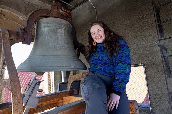 Zoe Perkins sits next to a large bell in the Memorial Building clock tower.