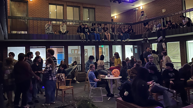 A large group of students gathered in a courtyard; some students sit along the railing on the second floor.