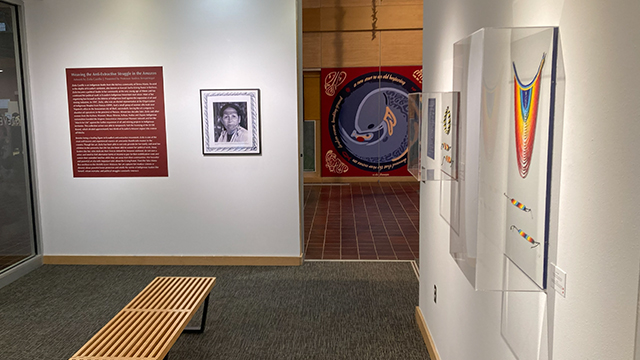 A gallery space with beaded artwork on one wall and a photo of the artist on another wall.