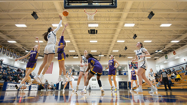 Basketball players in white/blue and purple/yellow playing in Sherwood Athletic Center.