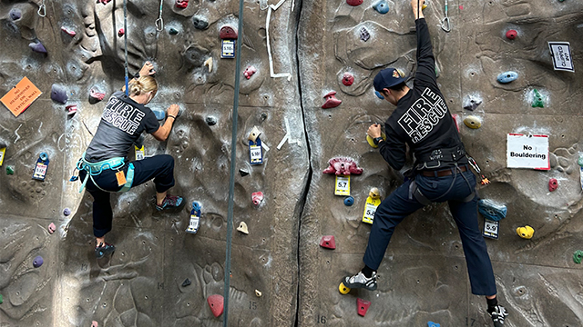 Two climbers wearing “Fire Rescue” t-shirts on a climbing wall.