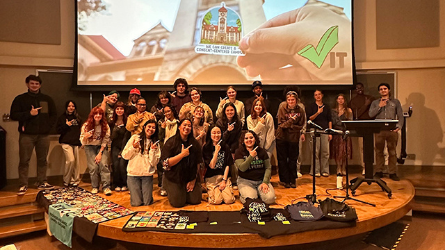 People on a circular stage making a check mark sign with their hands.