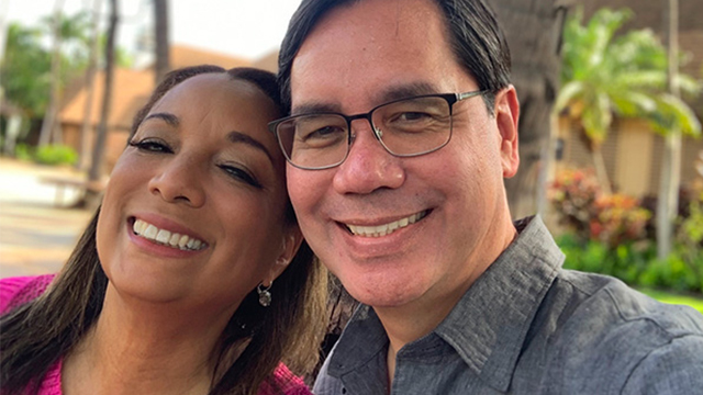 Selfie of Beth Long Saguinto and David M. Salaguinto with blurred palm trees in the background.