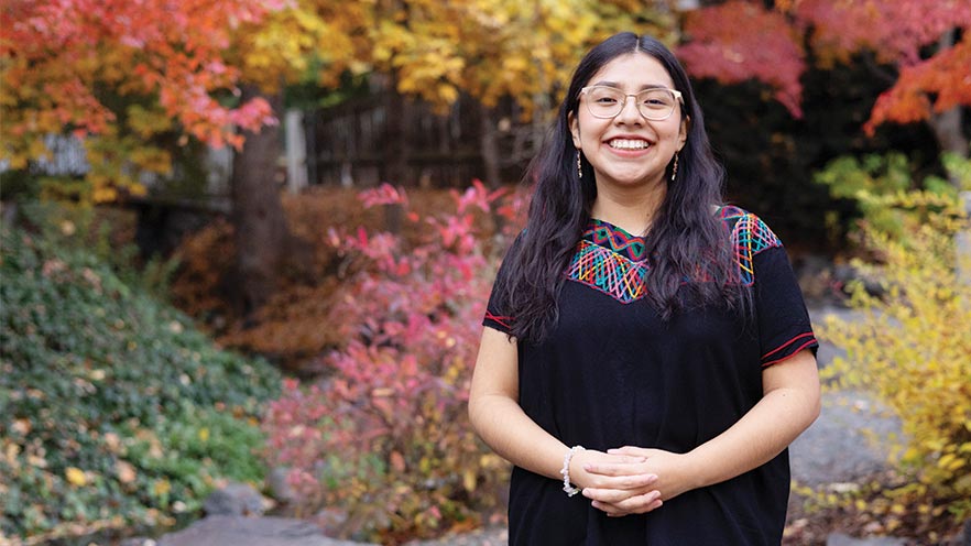 Eyleen Menchú Tuy stands outdoors, with fall foliage visible in the background.