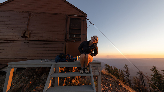 Arden Hunt sits on a platform overlooking a valley at sunset.