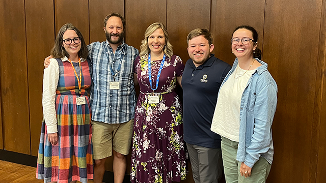 Five people pose together for a photo, several wearing lanyards around their necks.