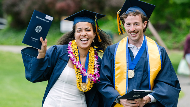 Two smiling Whitman graduates dressed in commencement regalia.