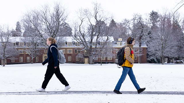 Two students walk in opposite directions across a snow-laden campus.