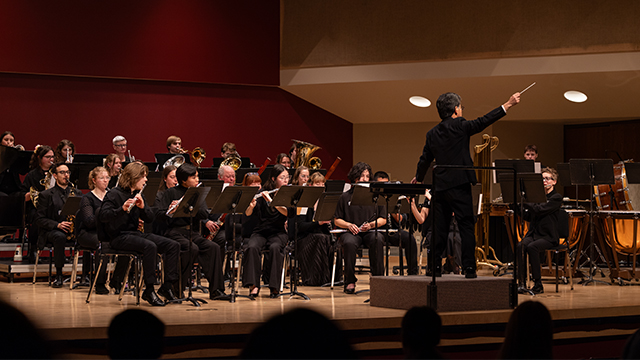 The Whitman Wind Ensemble playing on stage with the conductor raising a baton.