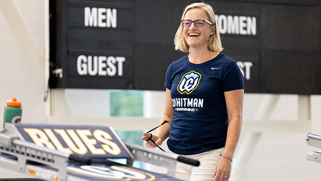 Jenn Blomme smiles standing next to a swimming starting block. 
