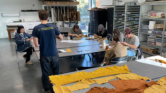 A group of people sit around a table making moccasins.