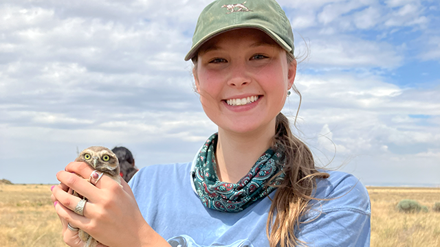 Lorelei Starr ’26 stand in an dry, grassy location, holding a small owl.