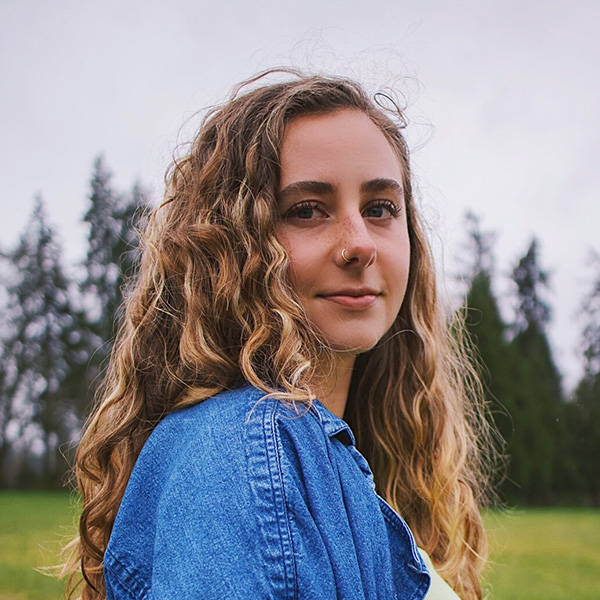 A woman angled at the camera with her shoulder forward, wearing a jean jacket 