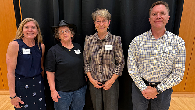 Four people pose for a photo in front of a dark background.