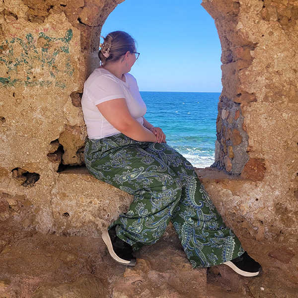 Angela Froming sits in a window in a stone wall looking out over the sea
