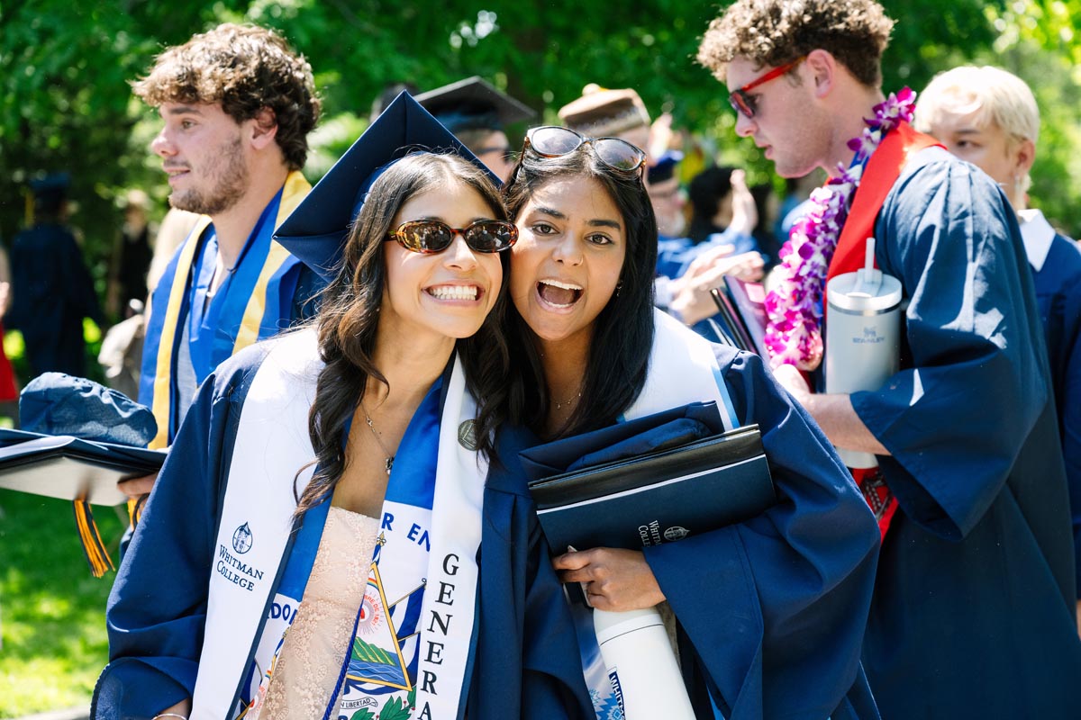 Two students wearing graduation regalia and smiling.