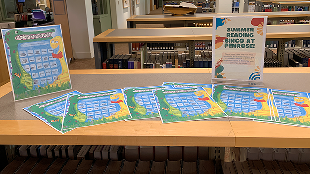 A bookshelf with a loose stack of flyers and a sign that reads “Summer Reading Bingo at Penrose”.