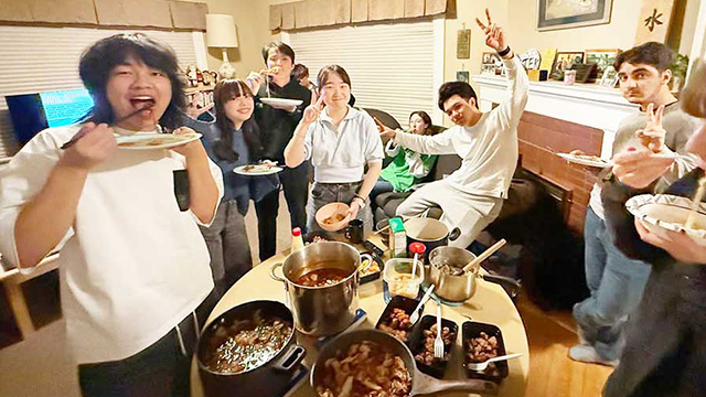 A group of students gather in a living room by a table filled with food.