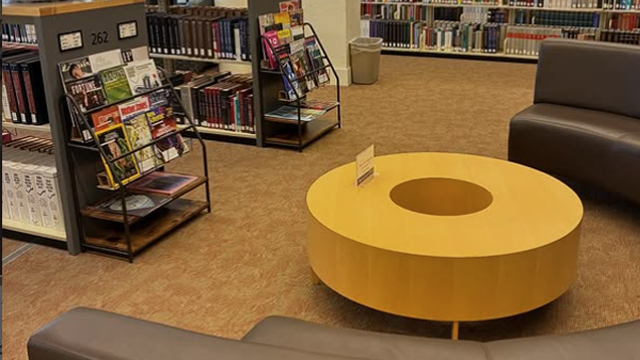 A circular table and seating area near two racks of magazines.