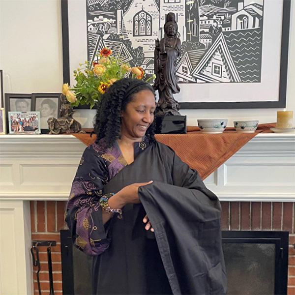 The rev. seigen johnson stands in front of a fireplace adjusting a black robe