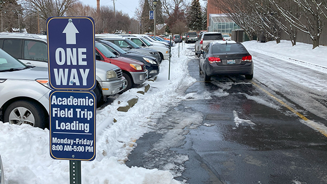 A sign with text: “Academic Field Trip Loading, Monday–Friday, 8:00 AM–5:00 PM” on the left. On the right, two cars parked in the designated loading zone.