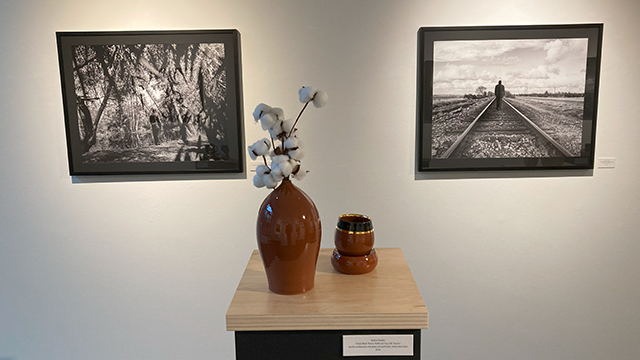 A brown vase on a small table in front of two black and white photographs hanging on a white wall.