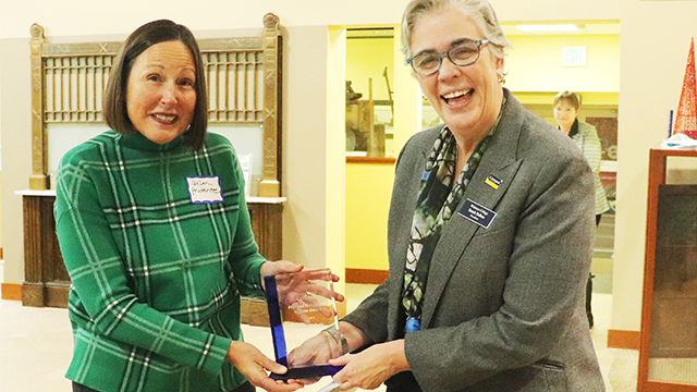 President Sarah Bolton (right) hands a glass award to Susan Prudente (left).