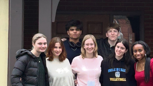 Seven students stand together under an archway.