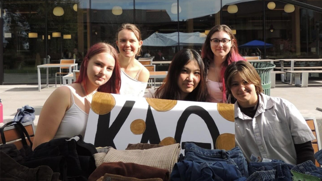 A group of students with a Kappa Alpha Theta sign in front of a table with folded clothes.