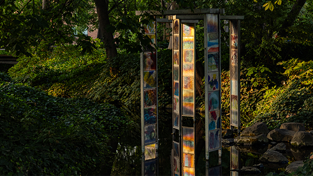 The “Topophilia Gates” sculpture, lit by the setting sun, sits in the bed of a stream.