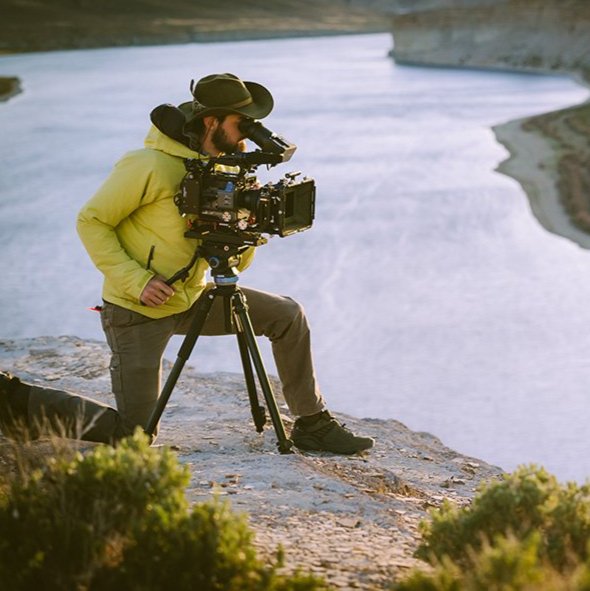 Ethan Parrish looks through the viewfinder of a camera set up on a bluff overlooking a river