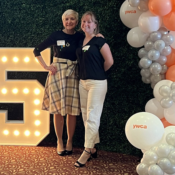 Anne-Marie Zell Schwerin '85 stands next to Kate Stoops '24 by a lighted &quot;25&quot; sign with orange, silver and white balloons that say 'YWCA'