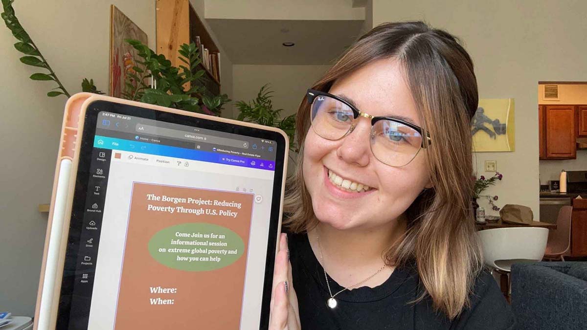 Tayva Anderson hold up a tablet that is displaying a “Borgen Project” event flyer.