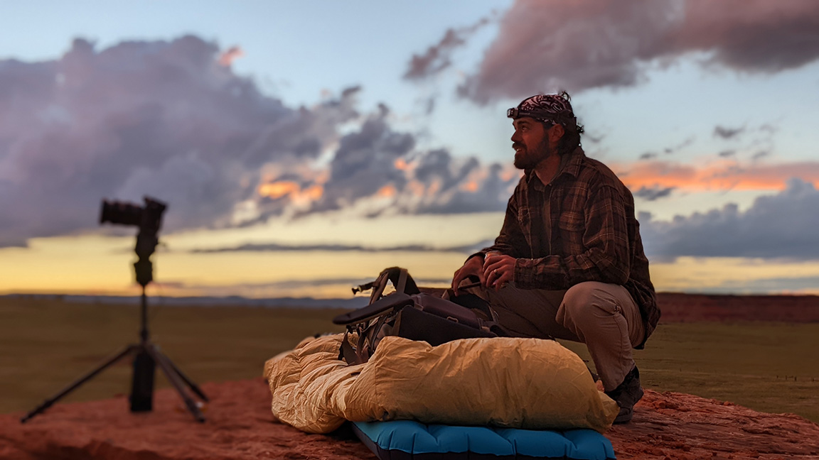 Ethan Parish outdoors with a sleeping bag, air mattress and photography equipment.