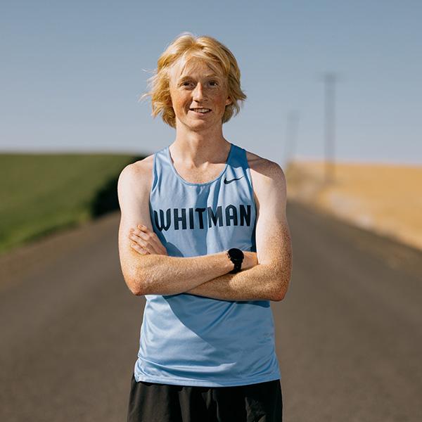 Jack McManus ’27 stands with crossed arms on a street next to a wheat field