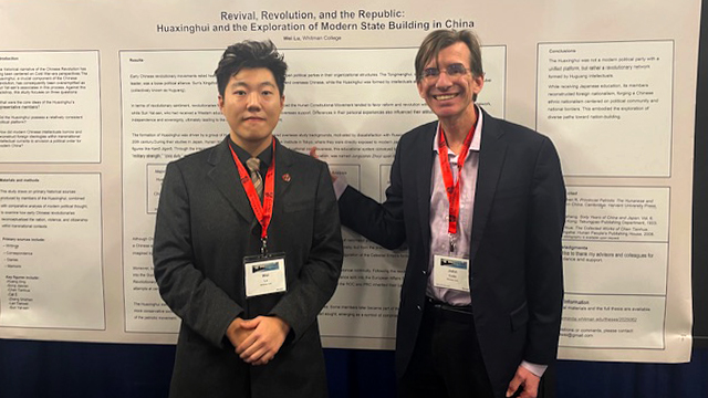 Wei Lu (left) and Professor of History John Cotts (right) stand in front of a large text-filled poster.